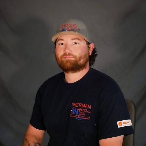 A man wearing a hat and a sherman shirt is sitting in a chair.