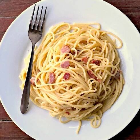 pasta with bacon on a white plate with a fork