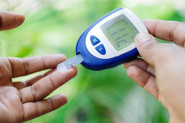 Person using a blood glucose meter by pricking their finger, displaying a reading, emphasizing diabetes management