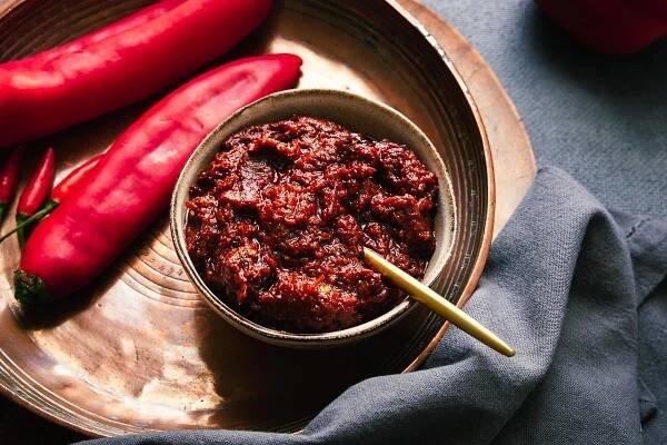 A ceramic bowl with homemade rose harissa and a golden serving spoon.