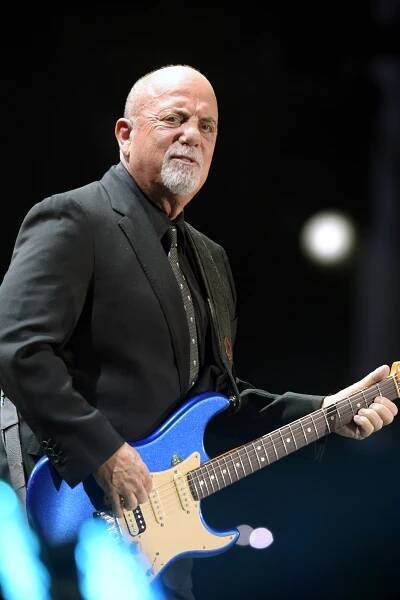 Billy Joel performing on stage with a blue electric guitar.