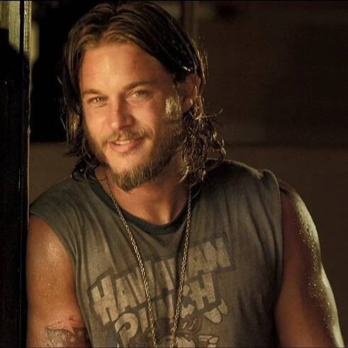 a man with long hair wearing a tank top and chain around his neck is looking at the camera