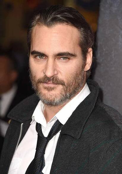 Joaquin Phoenix wearing a black and gray jacket over a loose tie and white button-down