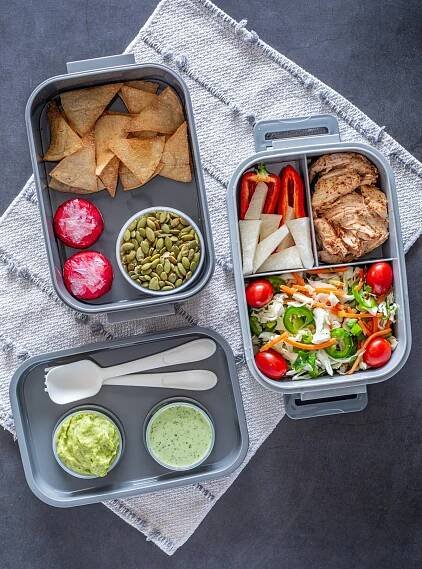 3 trays from the Mexican bento box with flatware, tajín chicken, tortilla chips, slaw, and sauces.