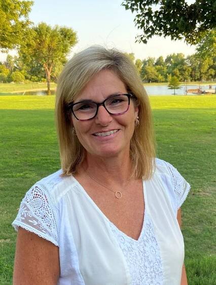 A woman wearing glasses and a white shirt is standing in a park.