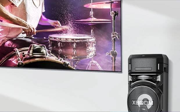 Televízor osadený na stene s reproduktorom LG XBOOM na pravej strane.