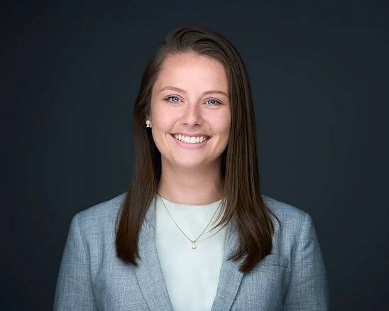 A woman in a suit and necklace is smiling for the camera.