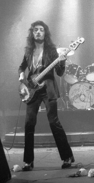 a man with long hair holding a bass in his hand while standing next to another person on stage