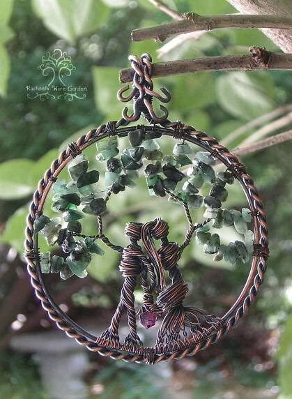 a wire wrapped tree ornament hanging from a branch with leaves and beads on it