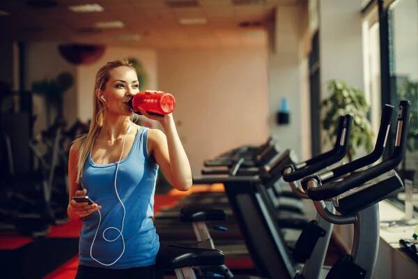 Aktivní žena pijící vodu po HIIT tréninku v posilovně