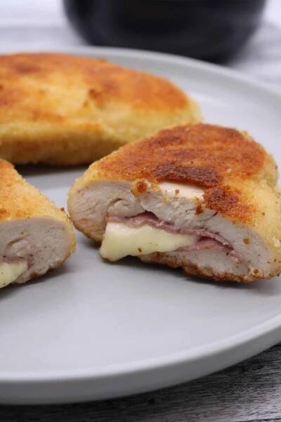 Close up of one chicken cordon bleu cut in half with whole one in the background on grey dinner plate