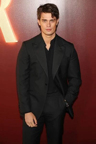 a man in a black suit and tie standing next to a red wall with the letter r on it
