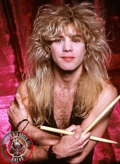 a man with long blonde hair holding two drumsticks in his hands and posing for the camera