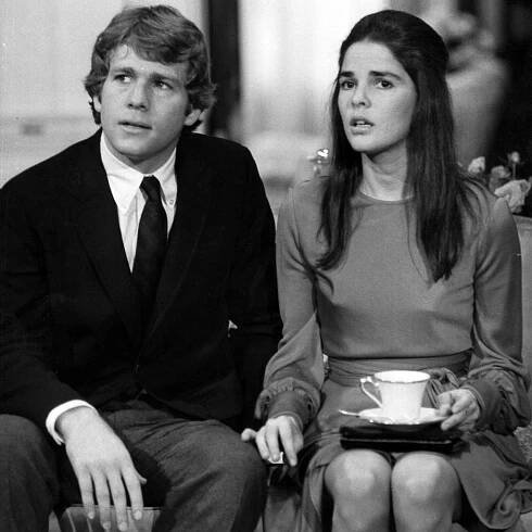 Ryan O'Neal sitting on couch with Ali MacGraw in a scene from the film 'Love Story', 1970