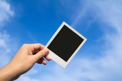 Ruka drží fotorámeček polaroid proti modré obloze — Stock obrázek