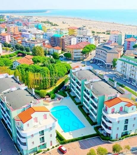 an aerial view of some buildings and a pool in front of the beach with cars parked nearby