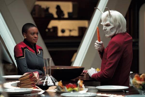 an alien with white hair and two stalk-like tentacles talks to a woman in a starfleet uniform