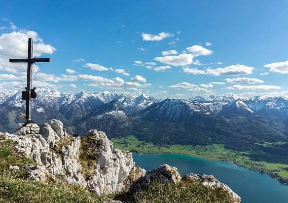 Sicht von einem Gipfel mit Gipfelkreuz auf den Wolfgangsee und der tiefen, teils verschneiten Berglandschaft des Salzkammerguts