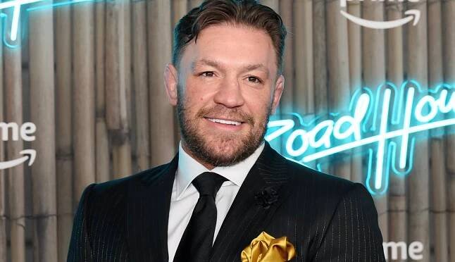 Conor McGregor pózuje, usmieva sa a pozerá do objektívu fotoaparáta na premiére filmu v obleku