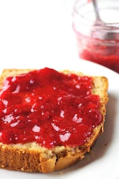 strawberry refrigerator jam spread on a slice of peanut butter bread with a jar of jam in the background