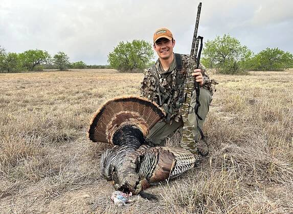A turkey hunter with an orange hat and a dead bird