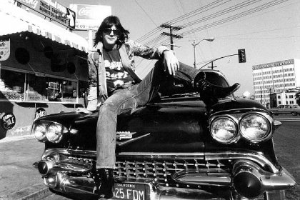 LOS ANGELES - CIRCA 1971: Singer/songwriter Gram Parsons poses for a portrait session wearing a t-shirt advertising his band Flying Burrito Bros. sitting on the hood of a Cadillac at Burrito King restaurant in circa 1971 in Los Angeles, California. (Photo by Ginny Winn/Michael Ochs Archives/Getty Images)