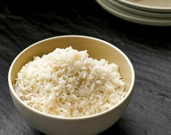 a white bowl filled with rice sitting on top of a black table next to plates