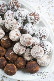 a white plate topped with lots of powdered sugar covered doughnuts and chocolate balls