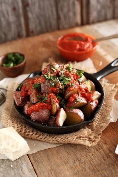 Skillet of Spicy Patatas Bravas with small bowls of extra sauce and parsley