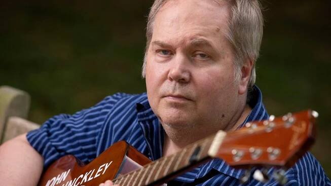 Portrait of John Hinckley Jr. holding his monogrammed guitar