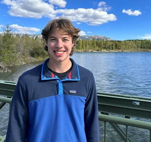 Young man wearing a blue sweater standing on a bridge above water.