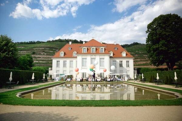 Elegant European manor house with orange tiled roof and reflecting pool surrounded by manicured gardens.
