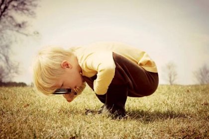Stáhnout - Malé dítě se předklání se v trávě, vyšetřuje něco s lupou. Vintage styl barva. — Stock obrázek