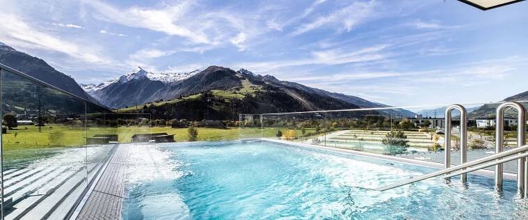Panoramapool mit Glaswand vor Berglandschaft unter blauem Himmel
