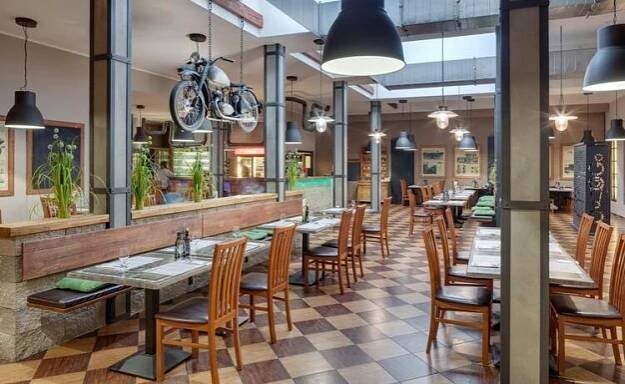WELLNESS HOTEL BABYLON - Restaurace s věšenou motorkou jako dekorací a dřevěnými židlemi.