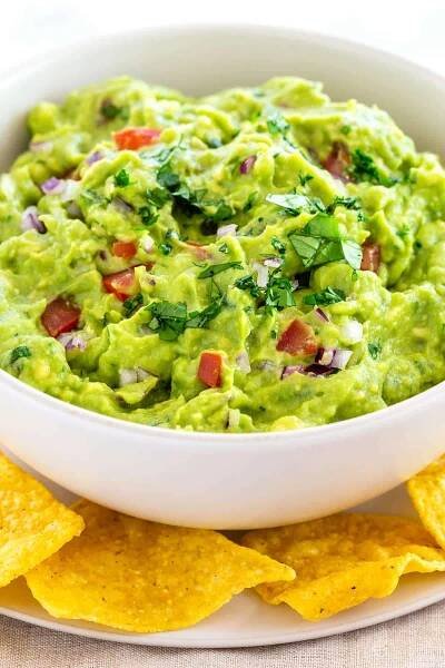 Guacamole in a white bowl served with tortilla chips.