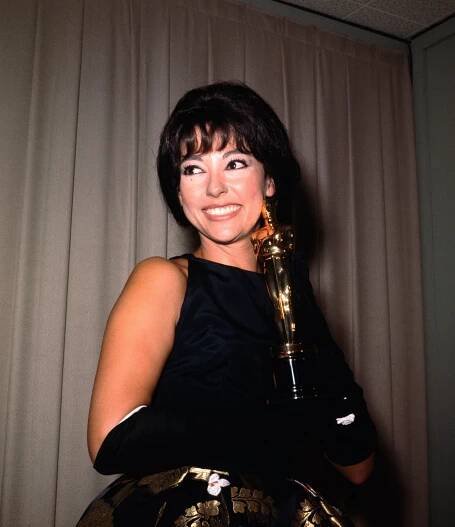 Rita Moreno in formal attire smiling, holding an award statuette