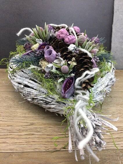 an arrangement of flowers and pine cones on a wooden table with white thread wrapped around it