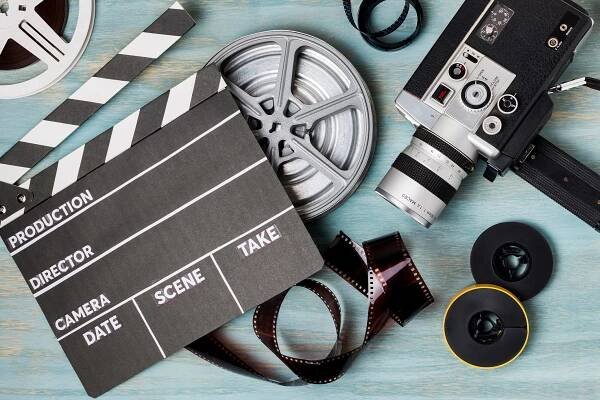 An elevated view of clapperboard; film reels; film strips and camcorder on blue wooden backdrop.
