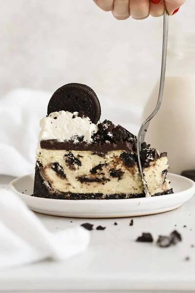 fork cutting into a slice of gluten-free Oreo cheesecake on a white plate