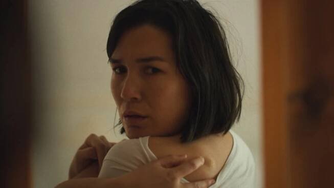 Zoë Chao looks over her shoulder into a mirror at a tick bite on her back in a still from 'The True Beauty of Being Bitten by a Tick'.