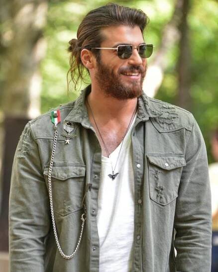 a man with long hair wearing sunglasses and a green jacket is smiling at the camera