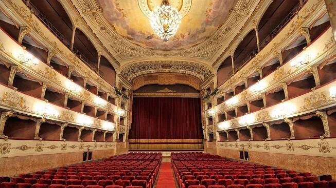 Empty theater with red chairs and chandelier hanging from ceiling