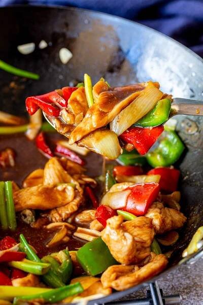 a silver spoon scooping chicken and peppers from a wok with a sticky brown sauce