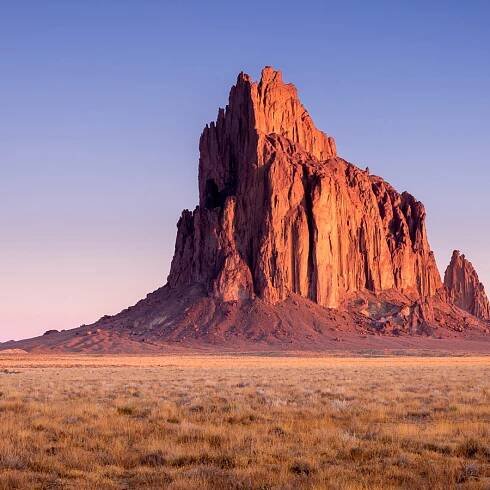 Tall cliff rising out of New Mexico dessert at sunrise.