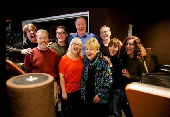 Group of smiling adults posing together in a recording studio