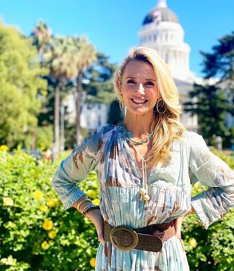 First Partner Jennifer Siebel Newsom smiles brightly in the sun in front of the state capitol.