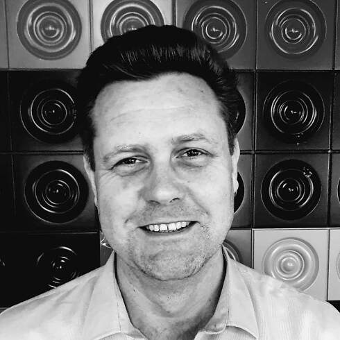 A professional portrait of a man smiling in front of a black and white textured wall, exuding confidence and positivity. This image may represent the leadership and approachable culture at Reborn Digital Marketing Agency, where individuals work with passion and creativity.