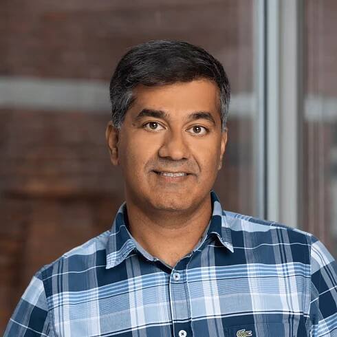 Vikas Mehta, ACV's Chief Operations Officer, smiles at the camera in a blue plaid button-down shirt.