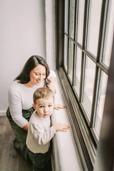 Parent and child standing by window in white room with natural lighting.